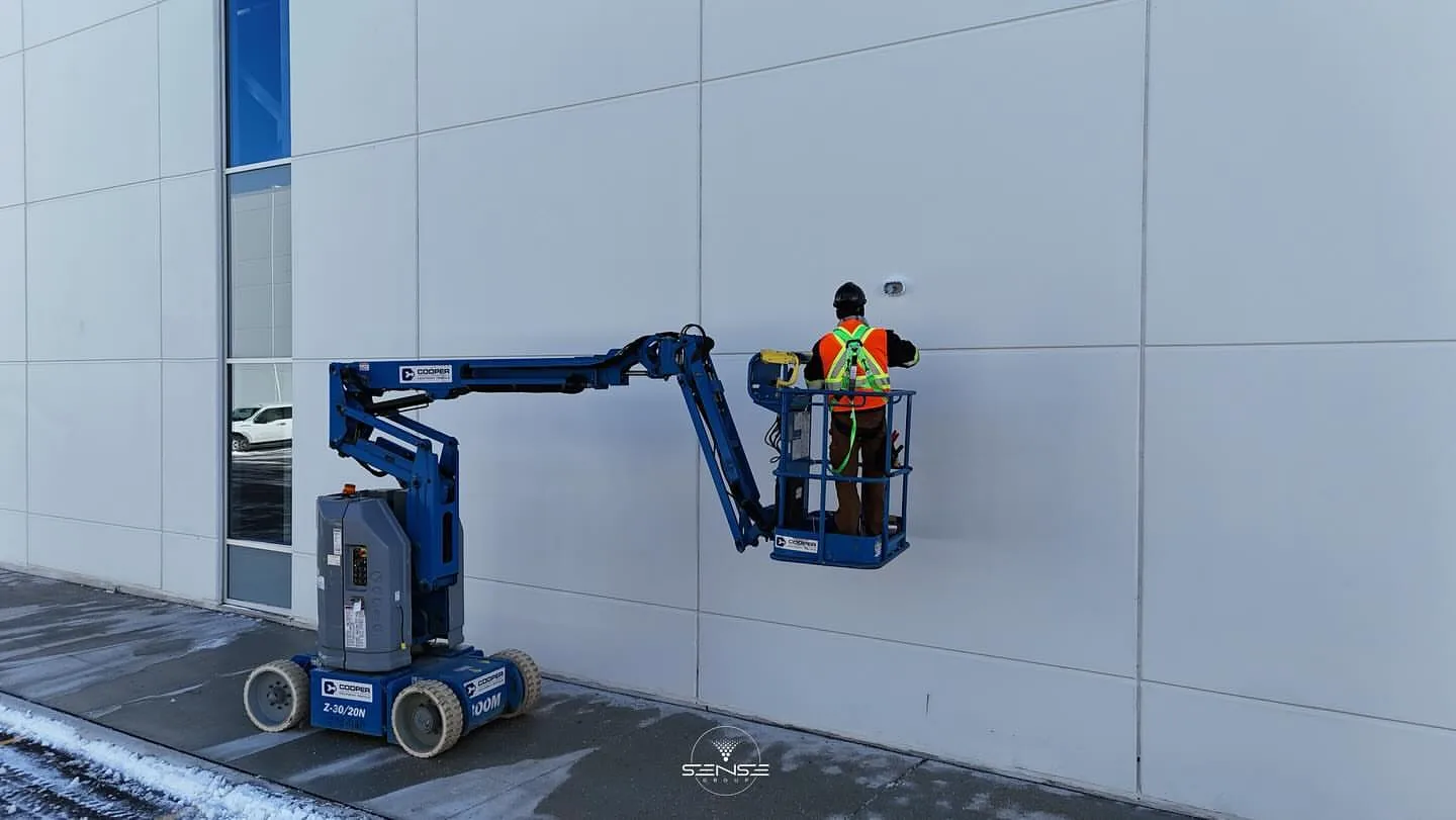 Technician on a boom lift installing a camera on a white warehouse exterior