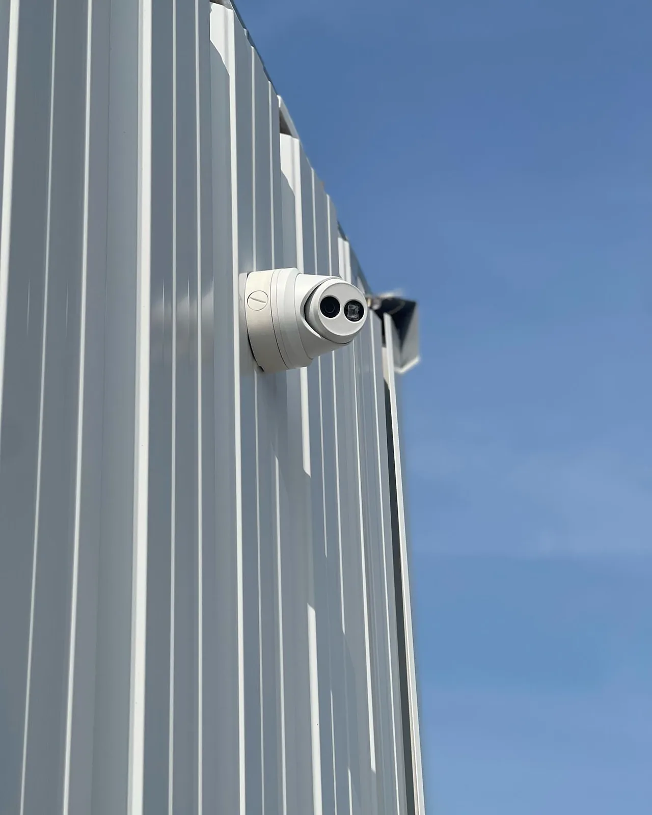 Turret camera on a corrugated metal wall against blue sky