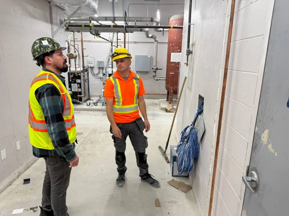 Two technicians in high-visibility vests talking in a mechanical room