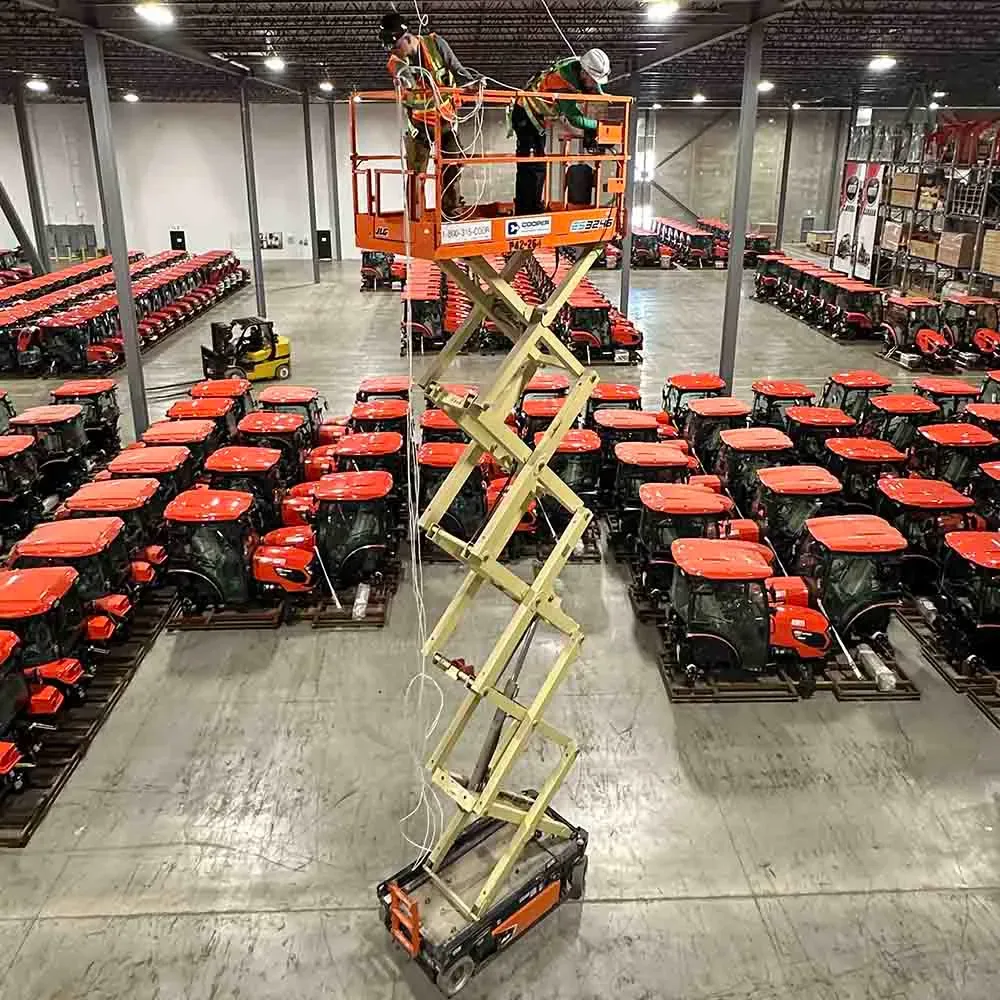 Scissor lift used to run network cabling in a warehouse full of red tractors