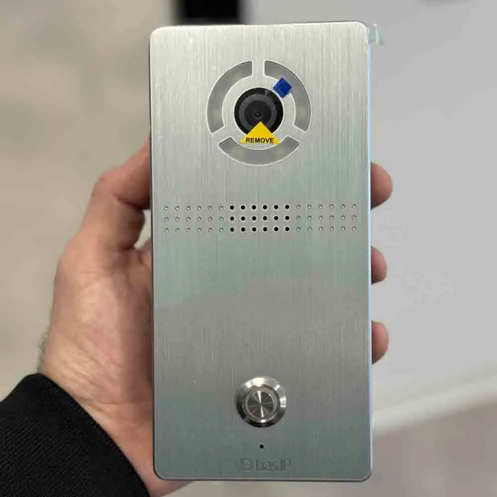Close-up view of a person holding a BAS-IP video intercom unit featuring a camera lens, speaker grill, and metallic doorbell button.