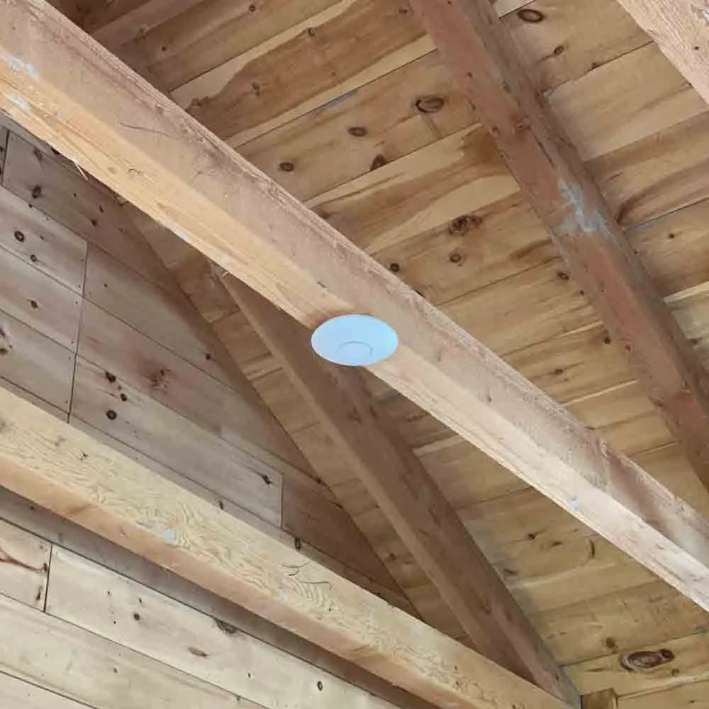 Wi-Fi access point mounted on the wooden ceiling beam of a rustic cabin, providing wireless connectivity throughout the space.