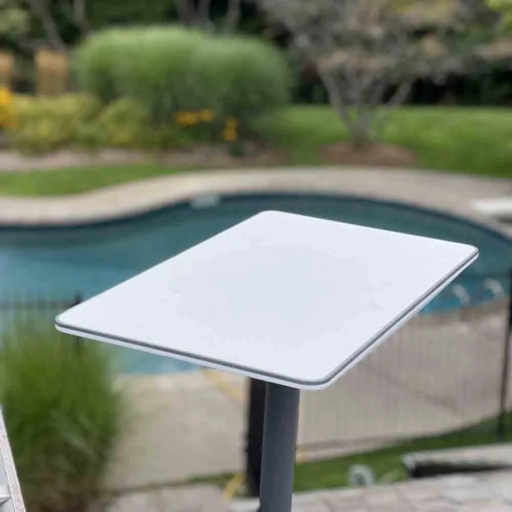 A white Starlink satellite dish mounted on a pole near a backyard swimming pool, surrounded by greenery and landscaping.