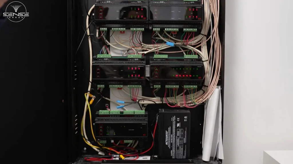 Open access control system cabinet showing multiple control modules, terminal blocks, backup power supply unit, and organized low-voltage wiring for door access and security management system.
