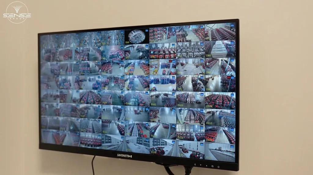 Wall-mounted security monitor displaying dozens of live CCTV camera feeds from a large warehouse facility, providing centralized video surveillance and real-time operational monitoring.