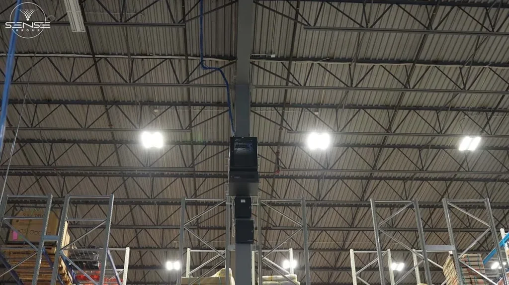 Wall-mounted network rack cabinet installed on a structural column inside a high-ceiling warehouse, with organized Ethernet cabling running overhead to support security cameras and network infrastructure.