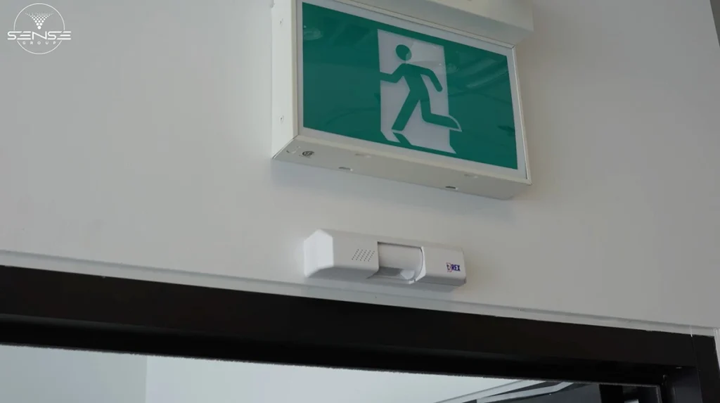 Motion detector sensor installed above commercial doorway with emergency exit sign in Ontario office building