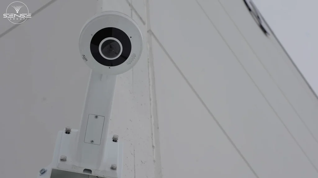 White fisheye CCTV security camera installed on a wall-mounted bracket, providing wide-angle 360-degree video surveillance for exterior building monitoring and perimeter security.
