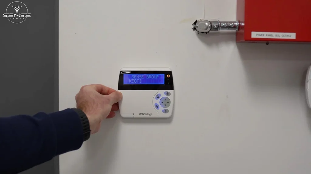 Wall-mounted ICT Protege security alarm keypad with LCD display being operated by a technician, used to arm and disarm a commercial security and access control system.