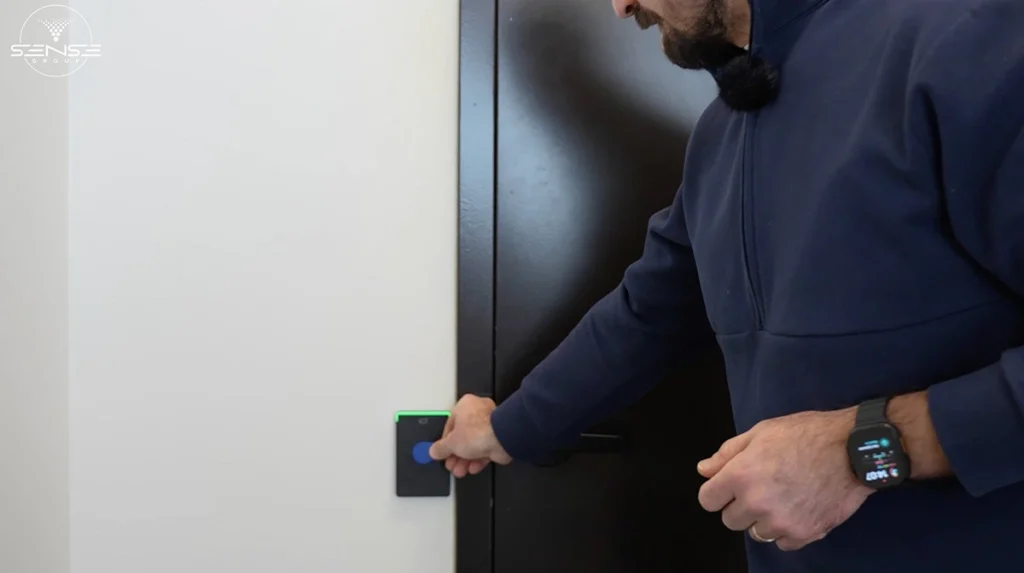 Man using an RFID access control card reader mounted beside a black office door, demonstrating secure key card entry system installation for controlled building access.